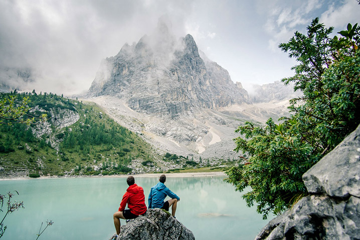 Dva muži v lehkých outdoorových bundách vyhlíží na horu v mlze.